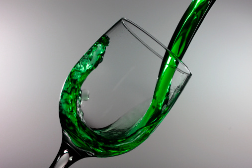 Green drinks splashing from a wine glass.