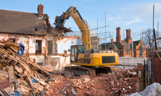 Destroying of old industrial building by modern high excavator destroyer at demolition site under blue sky on winter day