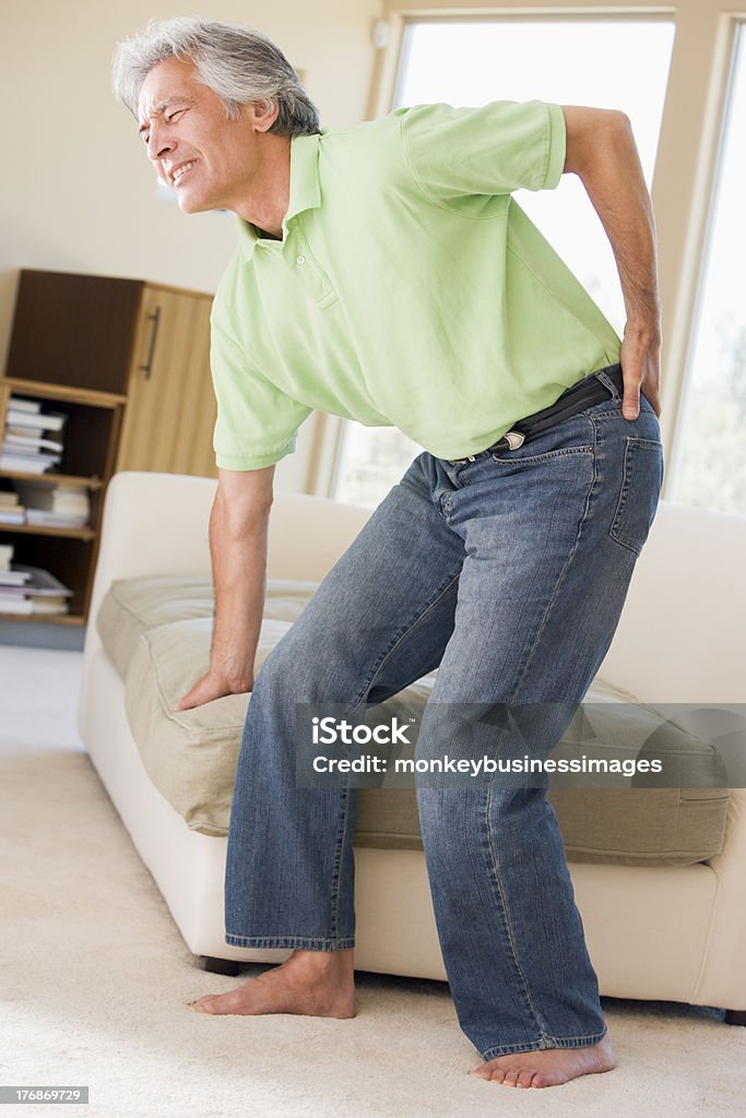 Man in a green polo shirt suffering back pain Man With Back Pain Trying To Sit On Sofa 50-59 Years Stock Photo