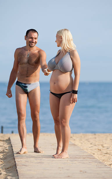 Attractive couple at the sea Middle aged man and young pregnant woman on the beach swimwear photos stock pictures, royalty-free photos & images