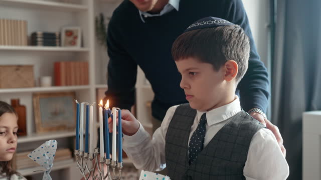 Close-up of a little boy lighting Menorah at the dining table