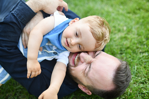 Smiling Father Showing Love To Baby Son On Playground Grass