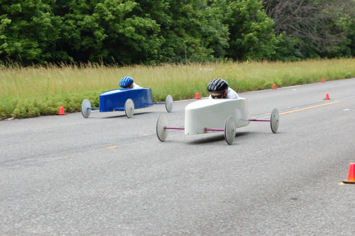 Two soap box derby drivers speed down the race track. Panning technique conveys speed by keeping focus on the cars while using a medium shutter to capture motion blur in the spinning wheels and panning blur in the background.
