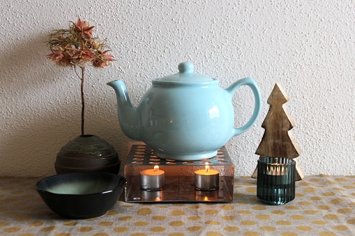 Teapot on teapot warmer with tea lights, tea cup. Autumnal accessories, for cosy autumn and winter evenings.