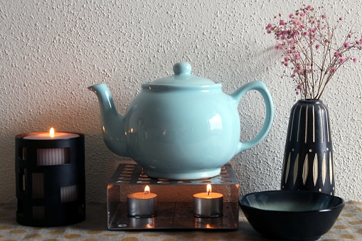 Teapot on teapot warmer with tea lights, tea cup. Autumnal accessories, for cosy autumn and winter evenings.