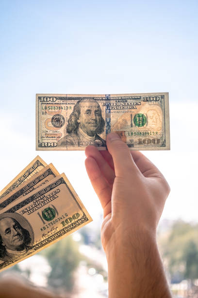istock A man checks the authenticity of a hundred dollar bill by shining a light from a window. 1768751415