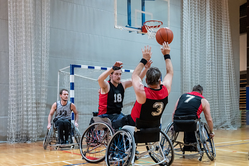 A team of disabled paraplegic basketball players in wheelchairs plays basketball in training. A basketball player throws the ball at the basket from under the basket.