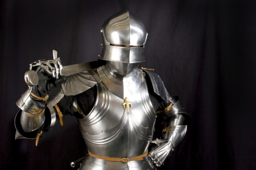 Knights in armor fights with swords. One of the knights stands on the muddy ground and the other one attacks while riding on a war horse. Castle in the background with soldier on guard.