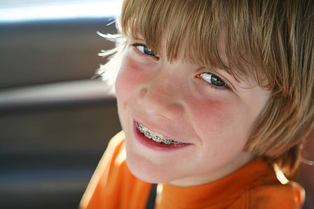 Summer smile Close up Portrait of boy with braces back lit from the summer sun. Shallow depth of field, focus on his eye. little boys blue eyes blond hair one person stock pictures, royalty-free photos & images