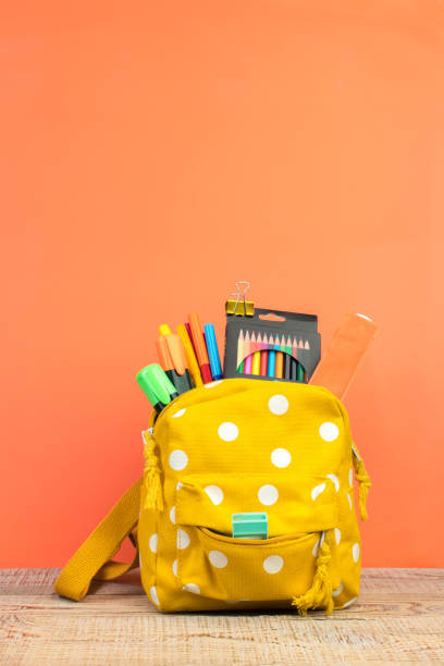 istock Yellow backpack with white polka dots with different colorful stationery on table. Orange background. Back to school. 1768780945