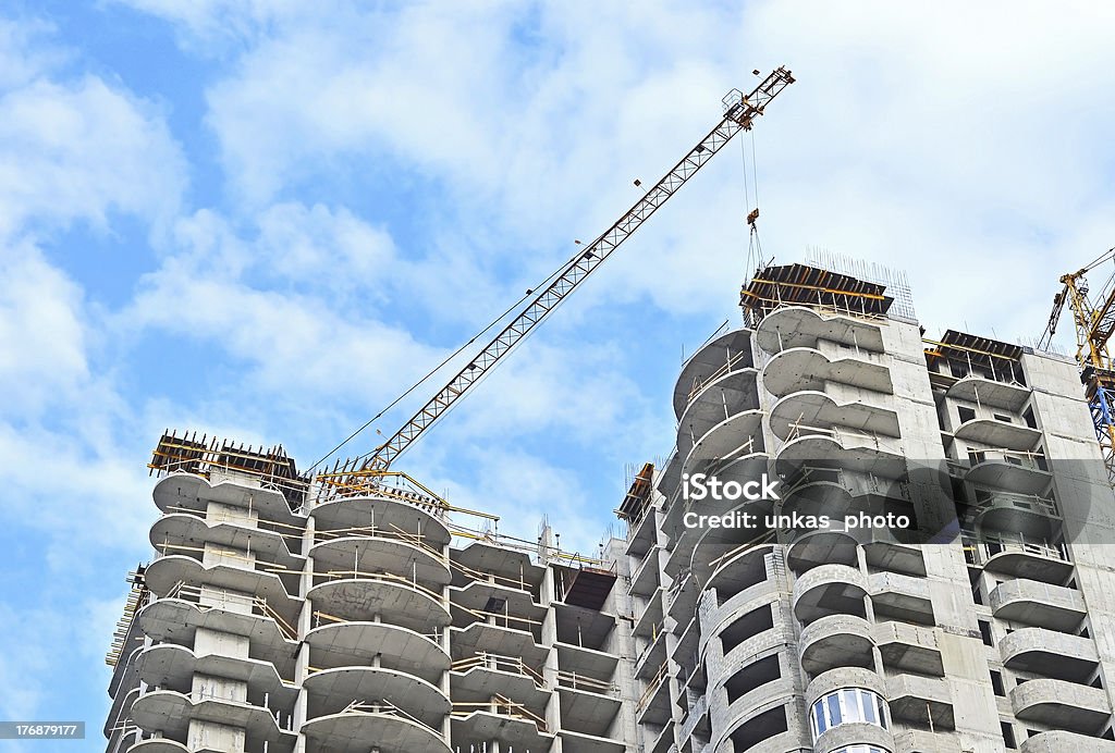 Crane and highrise construction site Building crane and building under construction against blue sky Apartment Stock Photo