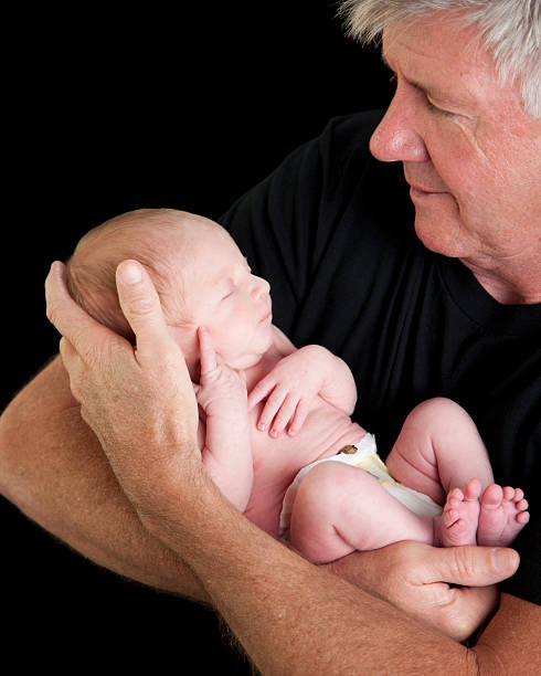 Proud Grandfather Holding Newborn Baby A proud grandfather looks down at his newborn baby grandson as he cradles him in his arms. sleeping grandpa stock pictures, royalty-free photos & images