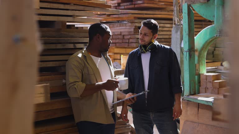 Diverse workers talking on their coffee break at a lumberyard while looking at a clipboard