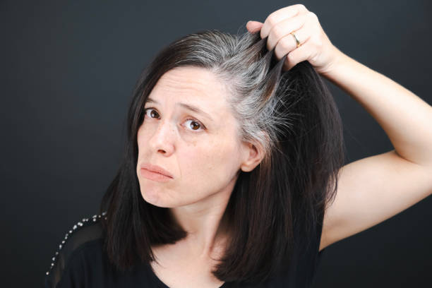 eine junge frau begutachtet die grauen haare auf ihrem kopf in einem spiegel auf schwarzem hintergrund. nahaufnahme der textur von grauem haar. - graues haar stock-fotos und bilder