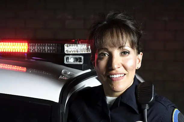 A Hispanic female officer standing in the night with her patrol car.