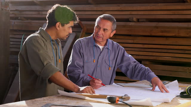 Supervisor and designer talking about the blueprint while writing on it at a furniture factory