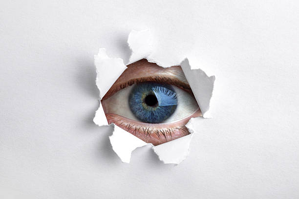 istock A blue eye looking through a ripped hole in white paper 176881995