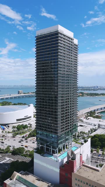 Establishing shot of impressive super-tall in Miami downtown on busy summer day. Breathtaking view of luxurious skyscraper with modern amenities on sea bay background