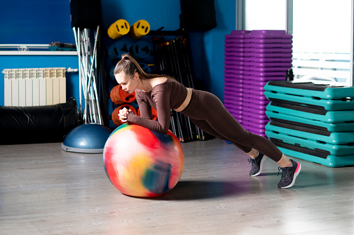 young female athlete doing exercises on a big rubber ball in a gym
