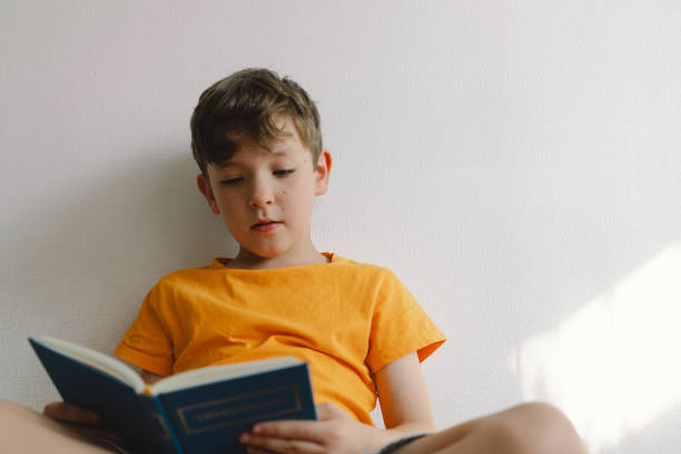 istock A cute boy is sitting on a soft ottoman reading a book. 1768858519