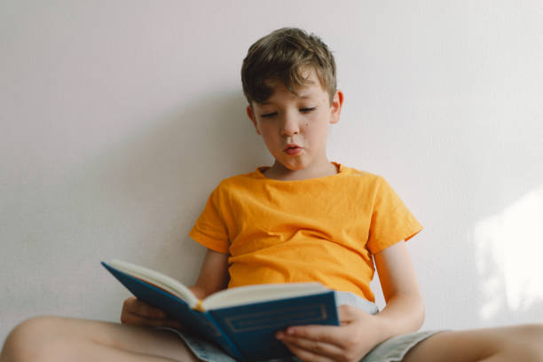 istock A cute boy is sitting on a soft ottoman reading a book. 1768858550