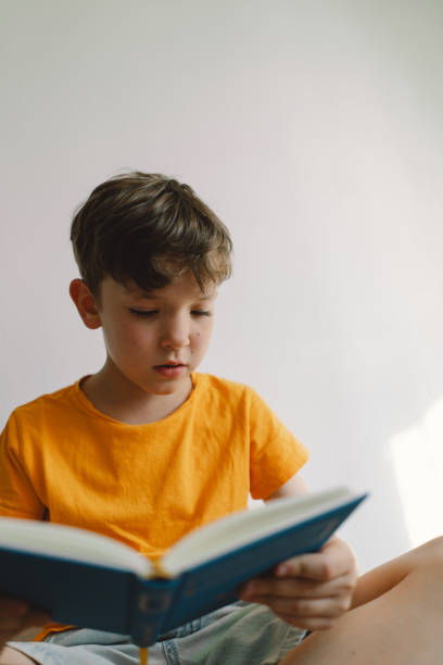 istock A cute boy is sitting on a soft ottoman reading a book. 1768859105