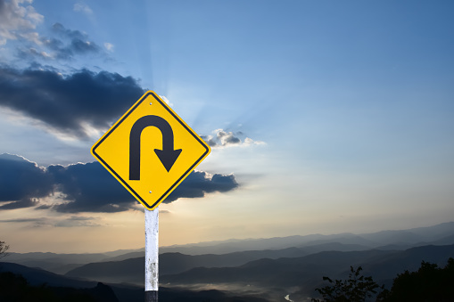 Traffic sign: Right U-turn sign on cement pole beside the rural road with sunset or sunrise background, copy space.