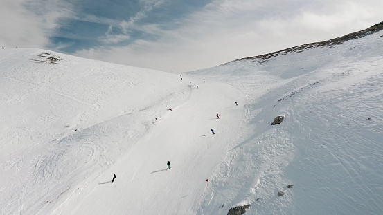 Livigno, Italy - February 21, 2022: People snowboarding skiing at ski resort. Skiers, snowboarders riding snowy mountain slope. Outdoor winter sport and scineric panoramic view. Aerial footage 4k