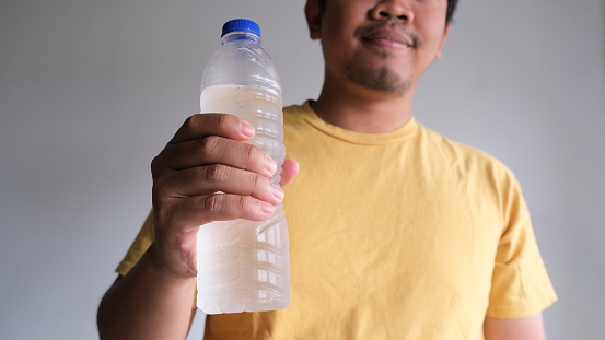Close up of Southeast Asian man holding a bottle of cold mineral water