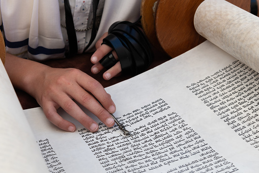 A reader uses a pointer to guide his hand and eyes across the text of a  Torah scroll during a Jewish prayer service.