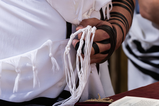 A Jewish man grasps the strings of his tallit or tzitzit while reciting the Shema Yisrael prayer during an Orthodox morning prayer service.