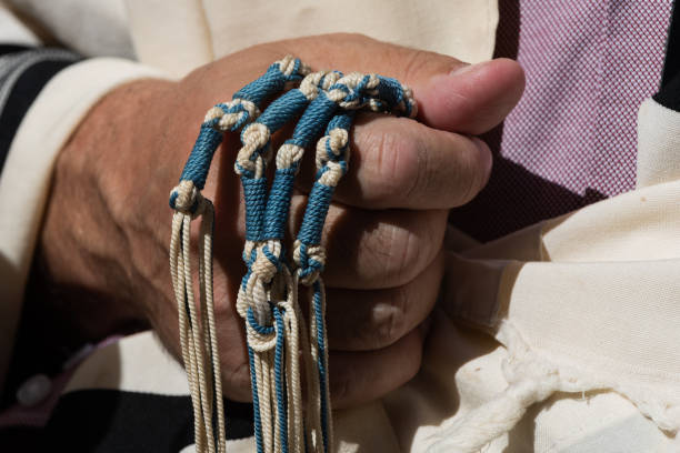 Holding techelet tzitzit during Jewish prayer A Jewish man holds the strings of his tallit or tzitzit while reciting the Shema Yisrael prayer during an Orthodox morning prayer service. jewish prayer shawl stock pictures, royalty-free photos & images