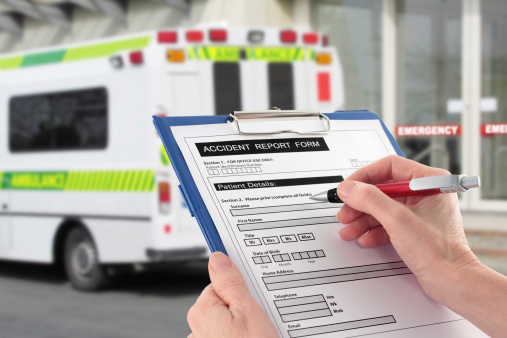 Hand completing an accident report form by an ambulance (medical emergency concept)