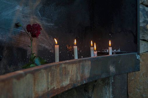 Burning candles in a dark room with a red rose in the foreground
