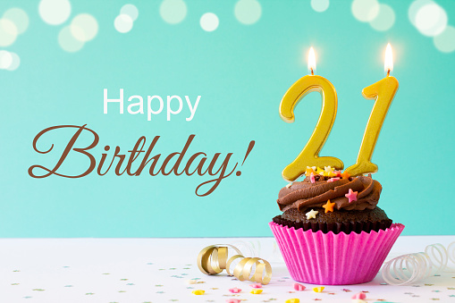 A chocolate buttercream cupcake with  sprinkles and gold 21st birthday candles. 
Shot  on a light blue background with defocused lights.