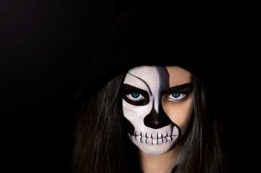 Portrait of a girl with makeup in the form of a skull and a hood on a black background