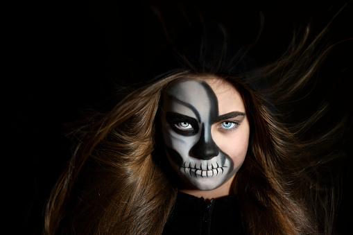 Portrait of a girl with makeup in the form of a skull and developing hair on a black background