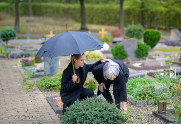 Daughter hugging her mother at the man's grave while caring for the grave Daughter hugging her mother at the man's grave in the cemetery on a cloudy cold day while caring for the grave annoying mother in law stock pictures, royalty-free photos & images