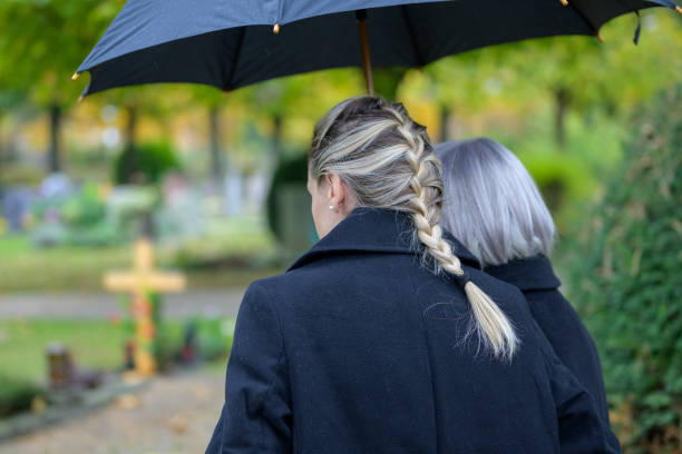 Close up rear view of daughter holding her mother on the way to the man's grave Close up rear view of daughter holding her mother in her arms on the way to the man's grave in the cemetery on a cloudy cold day annoying mother in law stock pictures, royalty-free photos & images