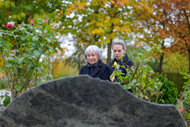 Close up of mother and daughter standing at the man's grave and looking down Close up of mother and daughter standing at the man's grave in the cemetery on a cloudy cold day and looking down annoying mother in law stock pictures, royalty-free photos & images