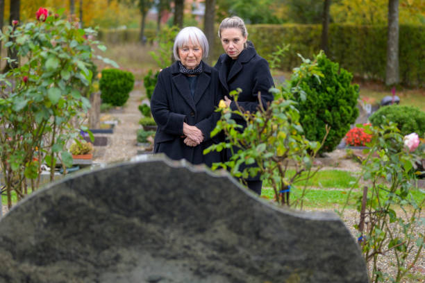 Mother and daughter standing at the man's grave and looking down Mother and daughter standing at the man's grave in the cemetery on a cloudy cold day and looking down annoying mother in law stock pictures, royalty-free photos & images