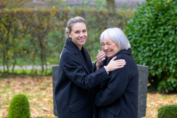 Close up of mother and daughter standing at the man's grave and seem to be happy Close up of mother and daughter standing at the man's grave in the cemetery and seem to be happy on a cloudy cold day annoying mother in law stock pictures, royalty-free photos & images