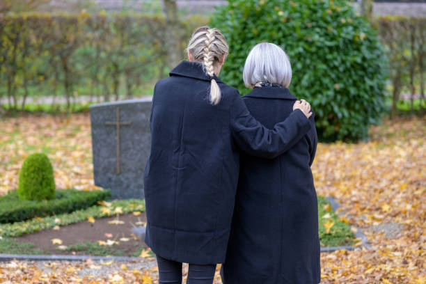 Daughter hugging her mother at the man's grave in the cemetery Daughter hugging her mother at the man's grave in the cemetery on a cloudy cold day annoying mother in law stock pictures, royalty-free photos & images