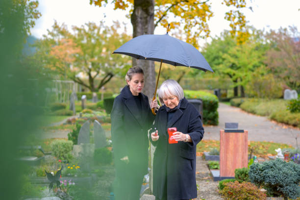 Mother and her daughter-in-law try to light a candle at her son's grave Mother and her daughter-in-law try to light a candle at her son's grave on a cloudy cold day annoying mother in law stock pictures, royalty-free photos & images