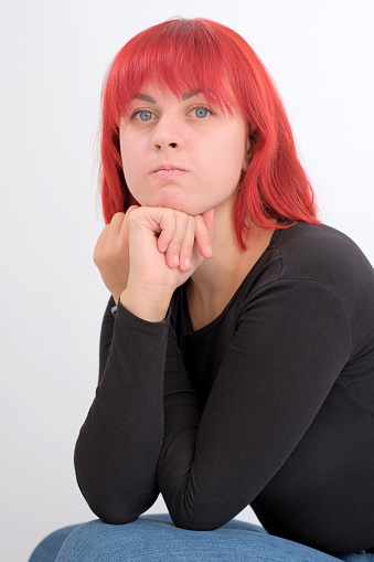 A young attractive woman with a short orange hairstyle in a black T-shirt and jeans posing in the studio on a white background.