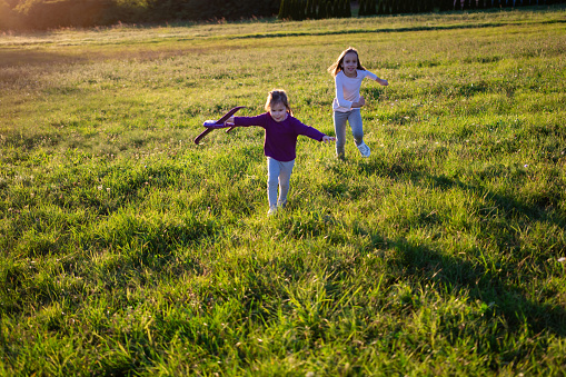 Playful girls flying airplane toy on field at sunset