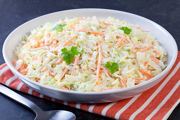 White plate of coleslaw with cloth and spoon on dark surface A bowl of coleslaw. coleslaw stock pictures, royalty-free photos & images