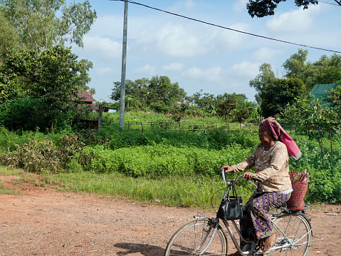 Siem Reap, Siem Reap, Cambodia-September 7, 2018: Cambodian woman with a large head scarf riding a bicycle on a rural road.