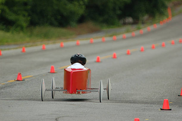 Red Race Car Redish orange soap box race car speeds down the track. Shallow depth of focus on car and driver whille forest background becomes a mellow muted blur. soapbox cart stock pictures, royalty-free photos & images
