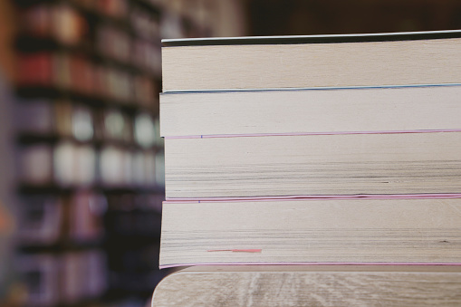 Stack of books on wooden desk in the library room background. Education and knowledge concept. Pile of books to read.